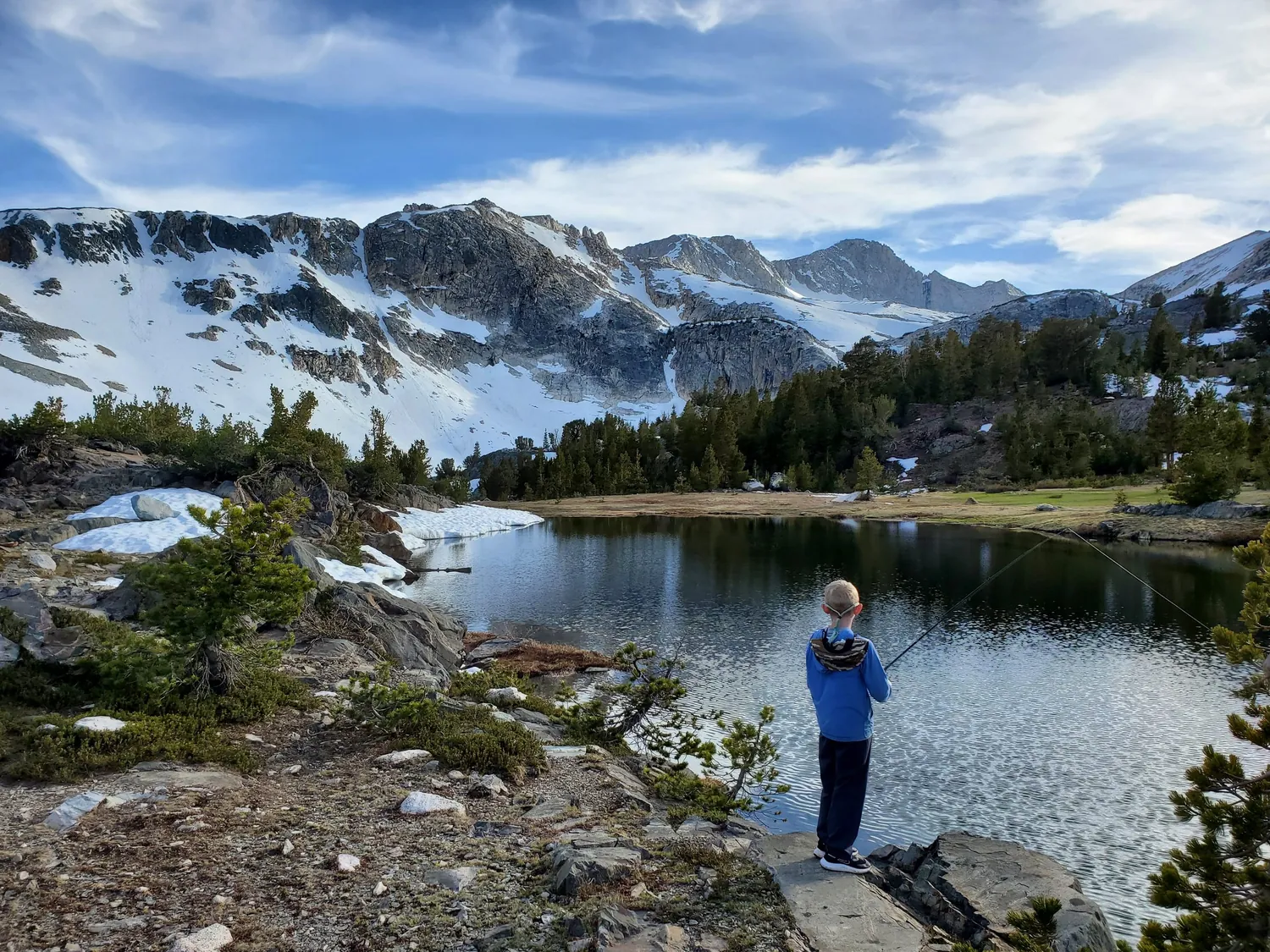Angler beside a clear alpine lake below snow-capped peaks